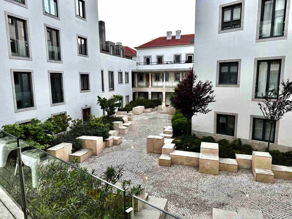 Photo of a cobblestone courtyard surrounded by plants, bushes, white apartment buildings 