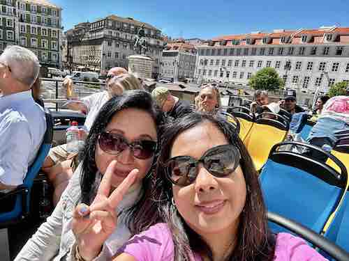Sightseers on an open top deck of a bus with two women wearing sunglasses on the foreground